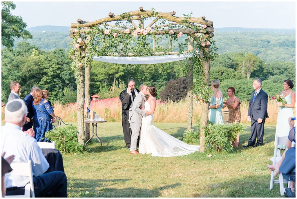 bride and groom first kiss under arch